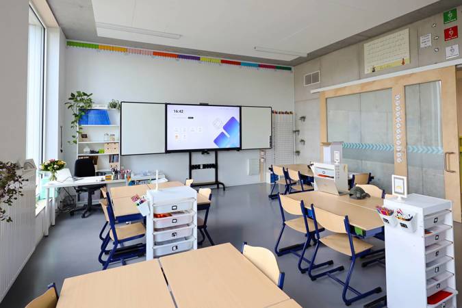 An empty classroom with several desks and chairs and an i3TOUCH interactive display.